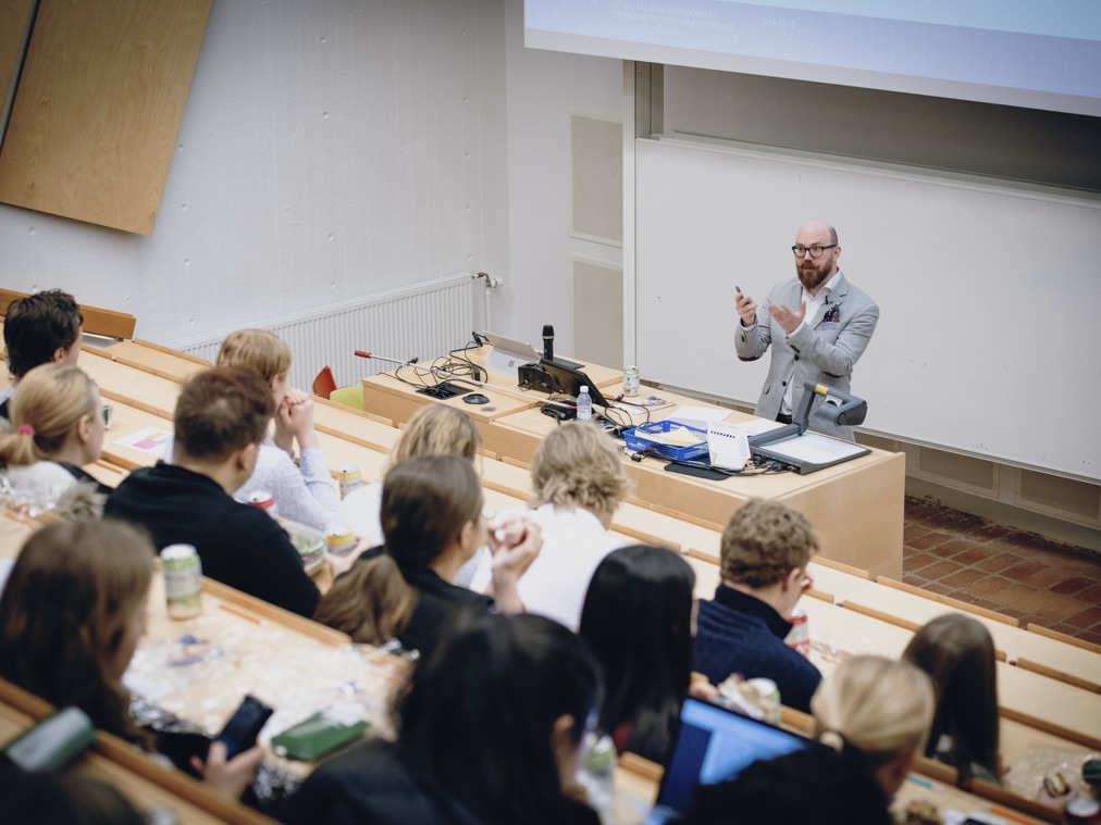 En man som står och undervisar i en föreläsningssal full av elever.