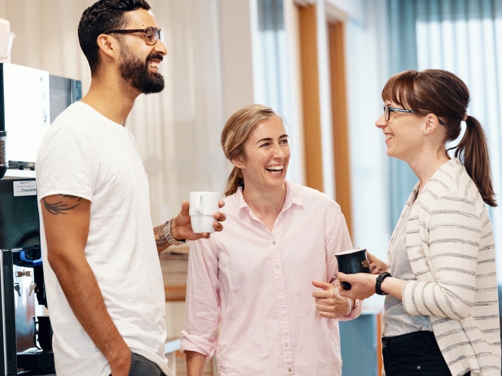 A group of people standing by a coffee maker.