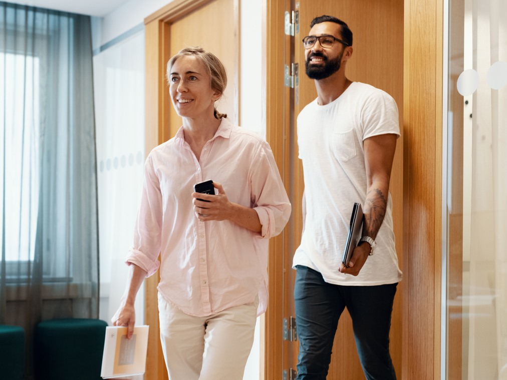 Två personer kommer ut från ett mötesrum med telefoner och datorer i händerna.