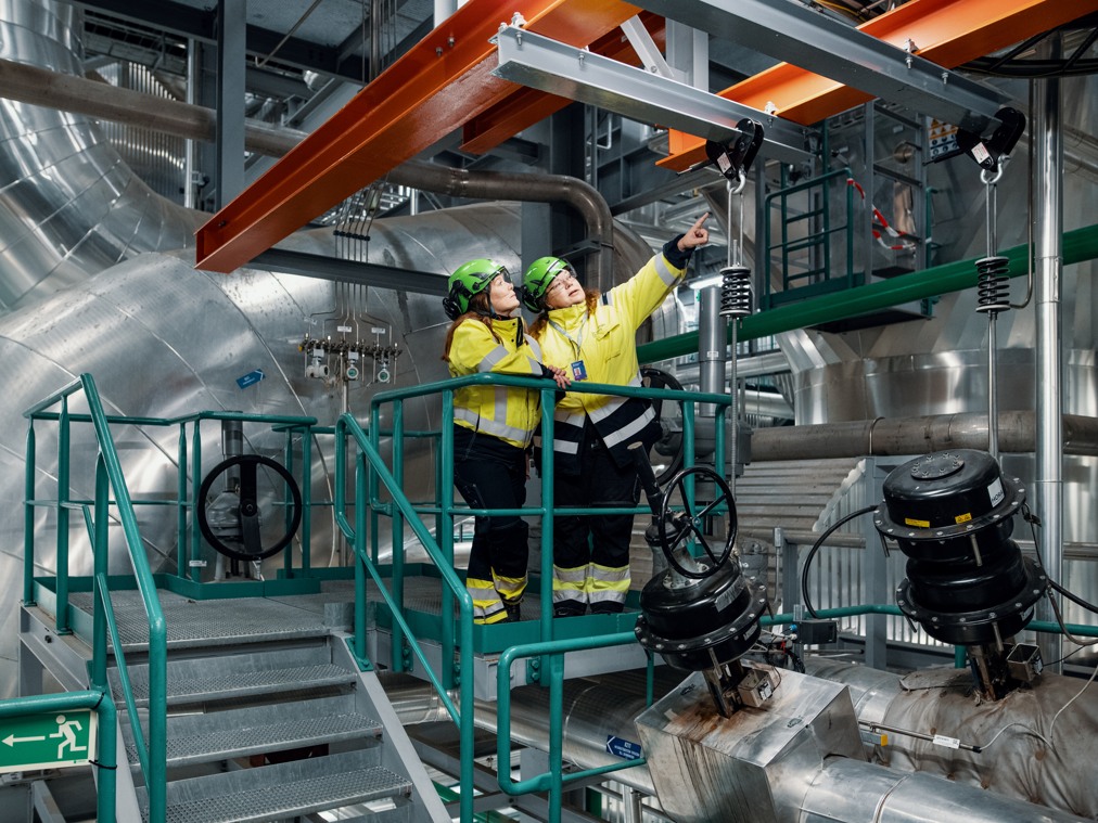 Två personer i varselkläder i en industrimiljö.