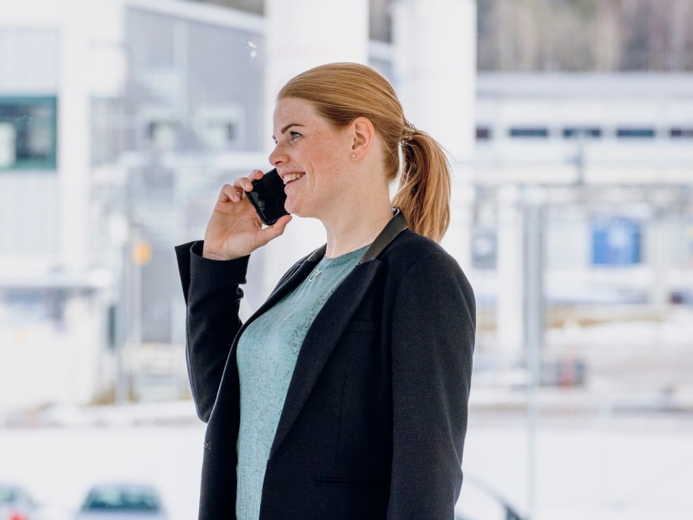 En kvinna pratar i mobiltelefon medan hon står framför en byggnad.
