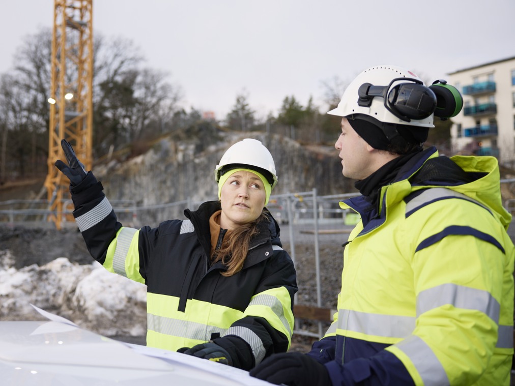 Två ingenjörer i varselkläder på en arbetsplats utomhus.