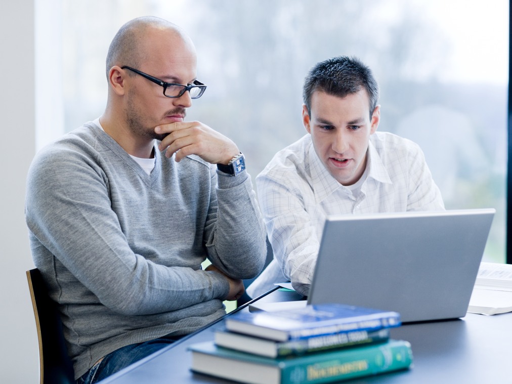 Två män sitter vid ett bord och tittar på en bärbar dator.