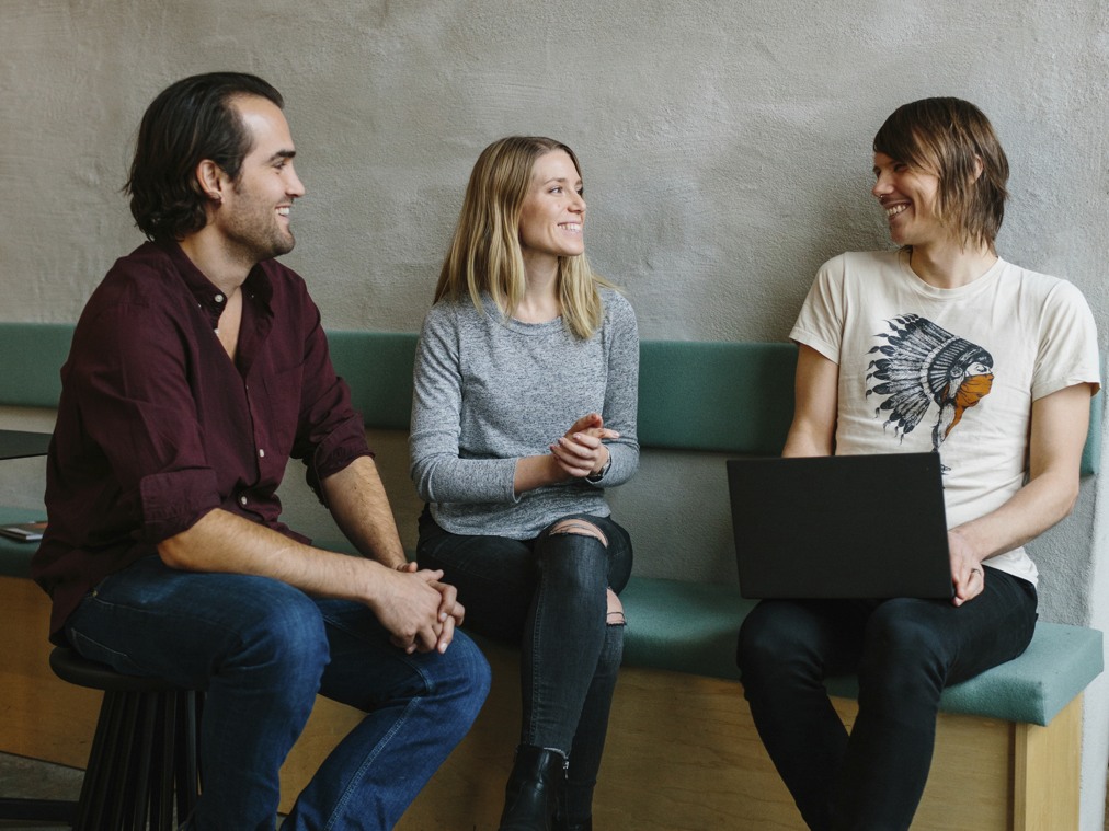 Tre personer sitter på en bänk med en bärbar dator.