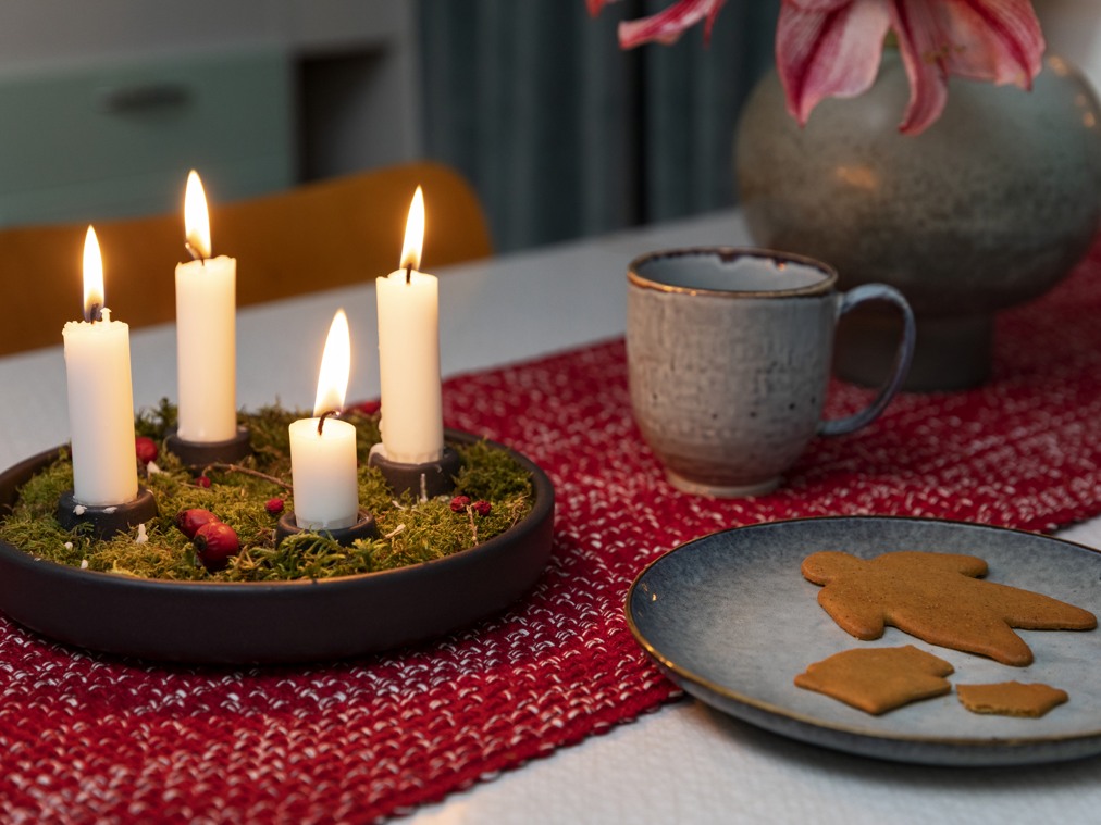 En tänd adventsljusstake, en kopp och ett fat med pepparkakor.