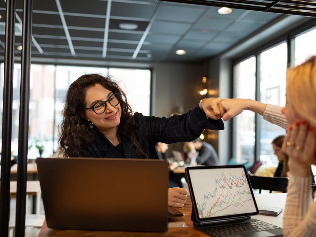 Two women with their laptops celebrating in a restaurant.