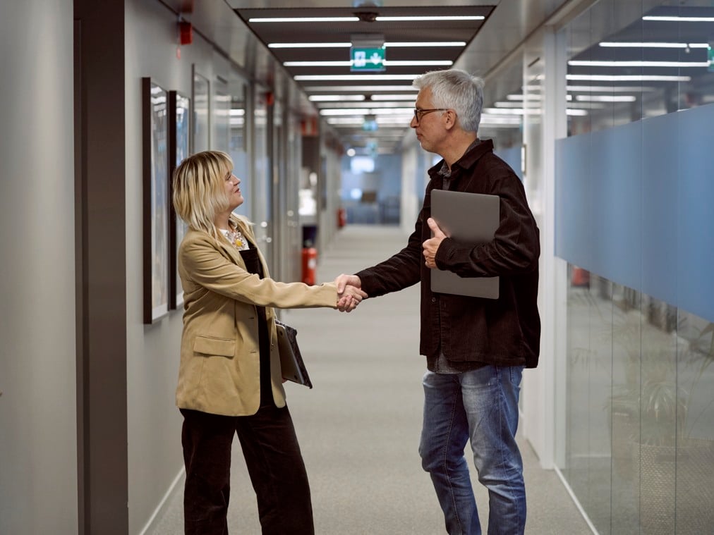 En man och en kvinna skakar hand i en kontorskorridor.