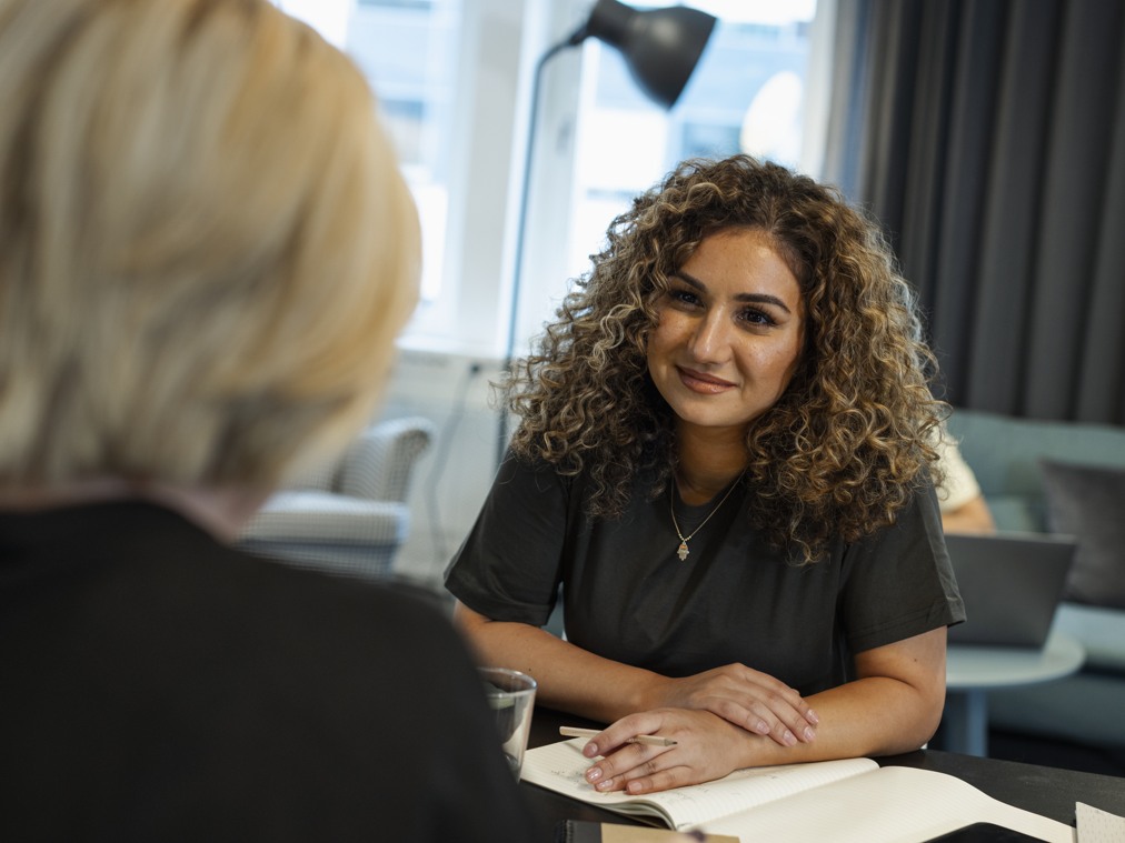 En kvinna sitter vid ett bord och pratar med en annan kvinna.