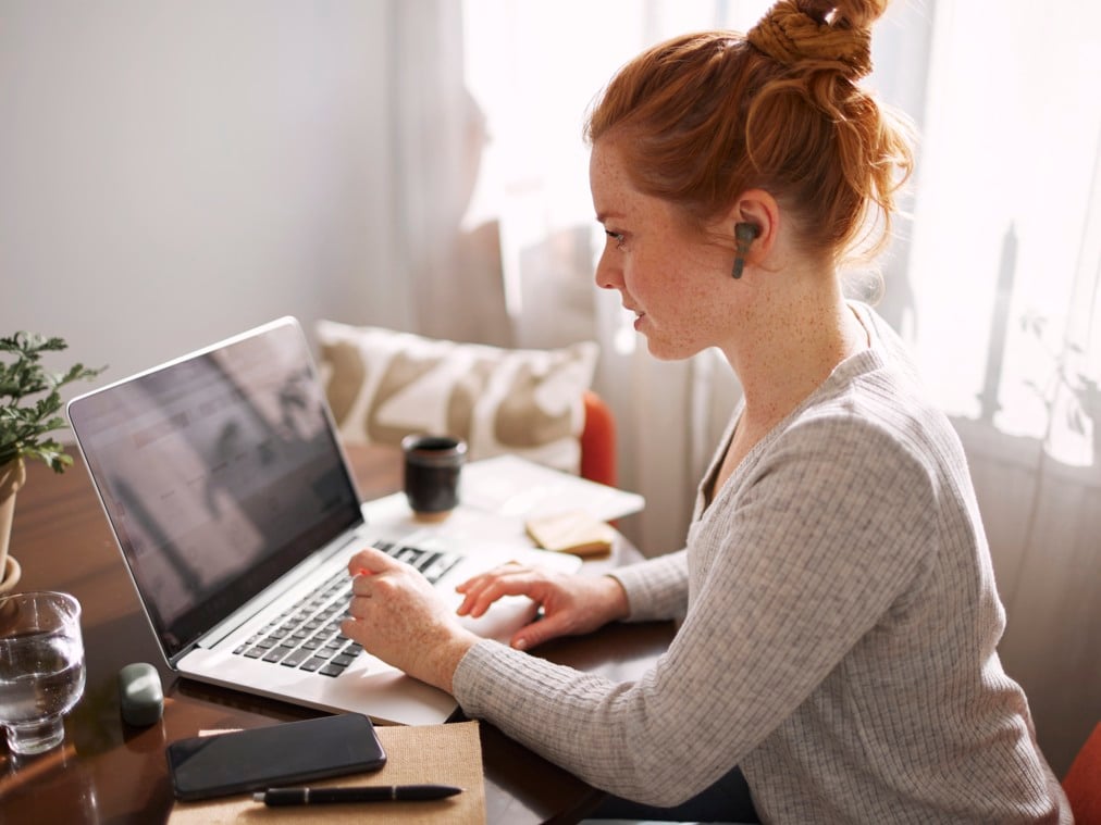 En kvinna sitter framför en bärbar dator och arbetar hemma.