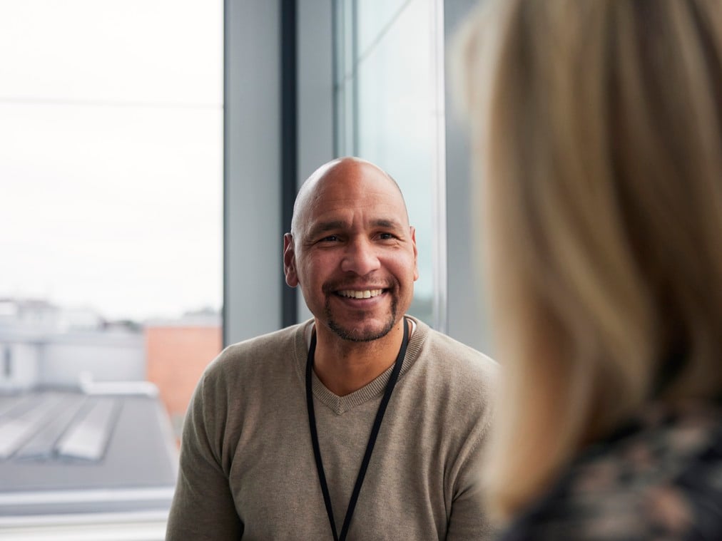 A smiling man sitting in front of a window next to a woman.