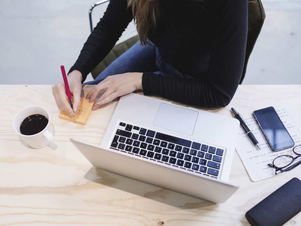 En kvinna sitter vid ett bord med en bärbar dator och en kopp kaffe.