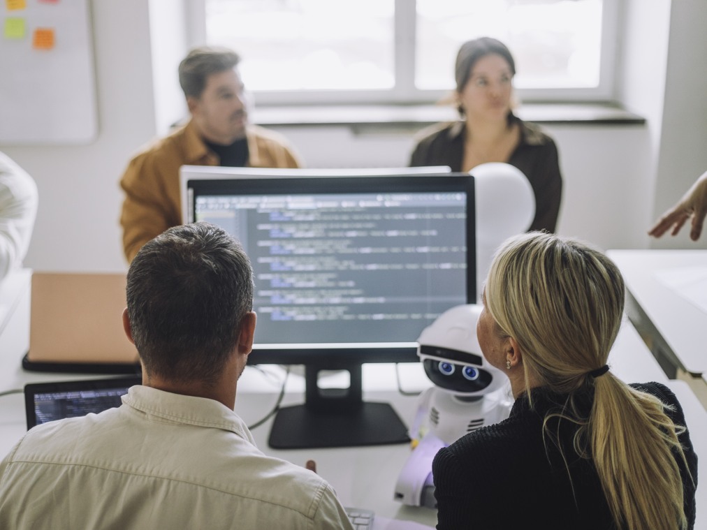 En grupp människor som sitter runt en dator och en liten robot.