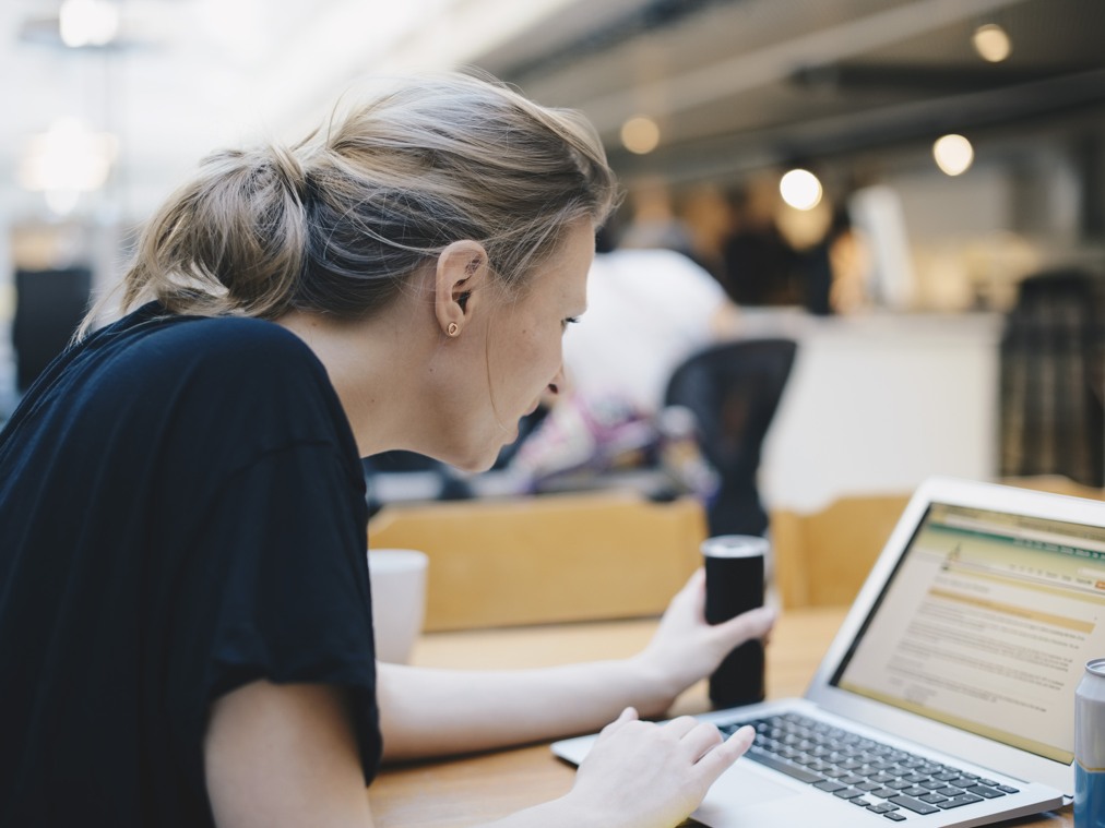 En kvinna sitter vid ett bord och använder en bärbar dator.